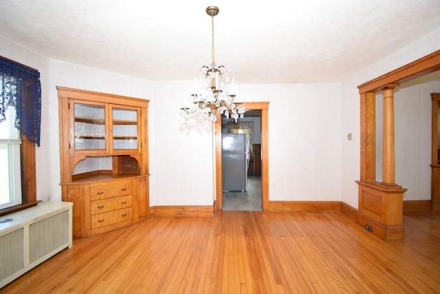 unfurnished dining area with baseboards, radiator, a chandelier, and hardwood / wood-style flooring