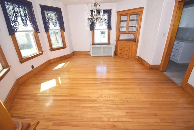 unfurnished dining area featuring baseboards, a notable chandelier, radiator heating unit, and light wood-style floors