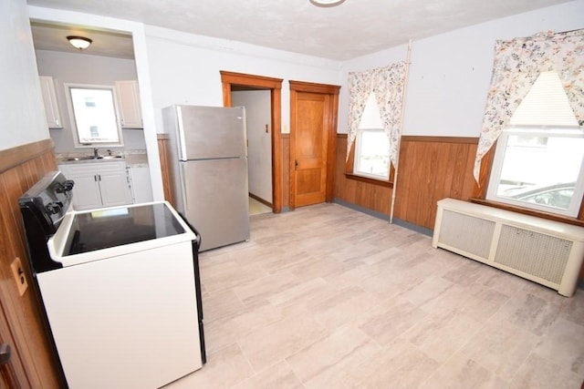 kitchen featuring electric range oven, wood walls, radiator heating unit, a wainscoted wall, and freestanding refrigerator