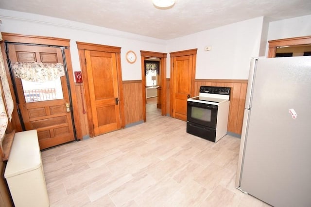 kitchen with electric range oven, brown cabinets, a wainscoted wall, freestanding refrigerator, and wooden walls