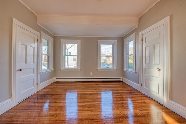 empty room with hardwood / wood-style flooring, ornamental molding, and a baseboard heating unit