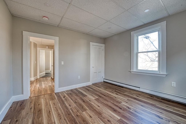 unfurnished room with hardwood / wood-style floors, a baseboard radiator, and a drop ceiling