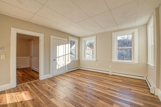 empty room featuring a paneled ceiling, wood-type flooring, and a baseboard heating unit