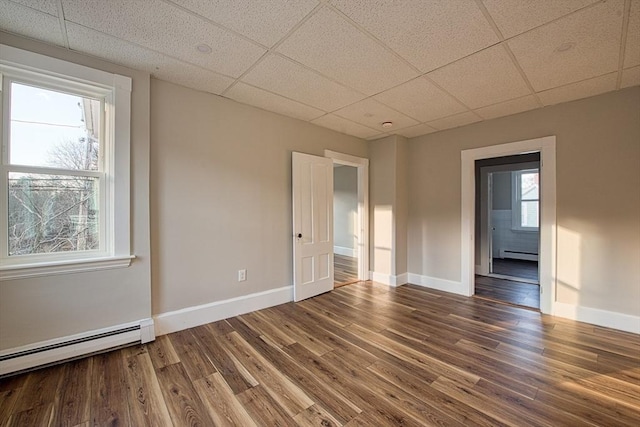 spare room featuring a paneled ceiling, a healthy amount of sunlight, baseboard heating, and dark wood-type flooring