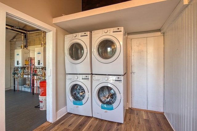 clothes washing area with hardwood / wood-style flooring, tankless water heater, stacked washer / drying machine, and water heater