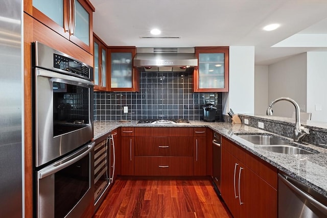 kitchen featuring wall chimney exhaust hood, stainless steel appliances, sink, and light stone counters