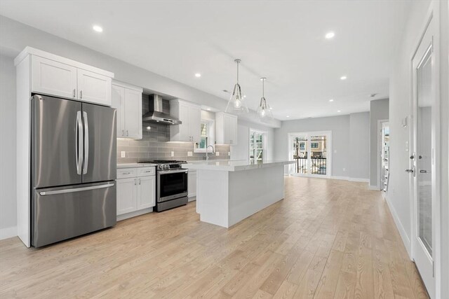 kitchen with light wood-type flooring, backsplash, appliances with stainless steel finishes, wall chimney exhaust hood, and light countertops