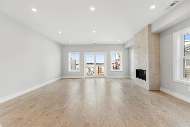 unfurnished living room with light wood finished floors, visible vents, a large fireplace, baseboards, and recessed lighting