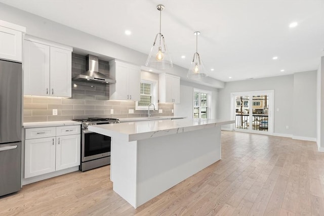 kitchen with light wood-style flooring, stainless steel appliances, white cabinets, wall chimney exhaust hood, and tasteful backsplash