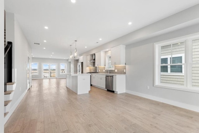 kitchen featuring a kitchen island, open floor plan, stainless steel appliances, white cabinets, and wall chimney range hood