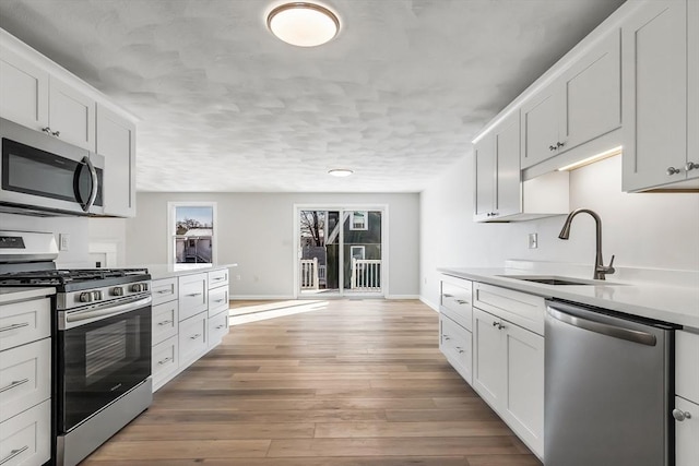 kitchen with stainless steel appliances, white cabinetry, sink, and hardwood / wood-style floors