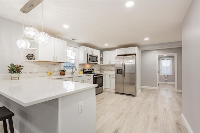 kitchen with sink, stainless steel appliances, kitchen peninsula, decorative light fixtures, and white cabinets