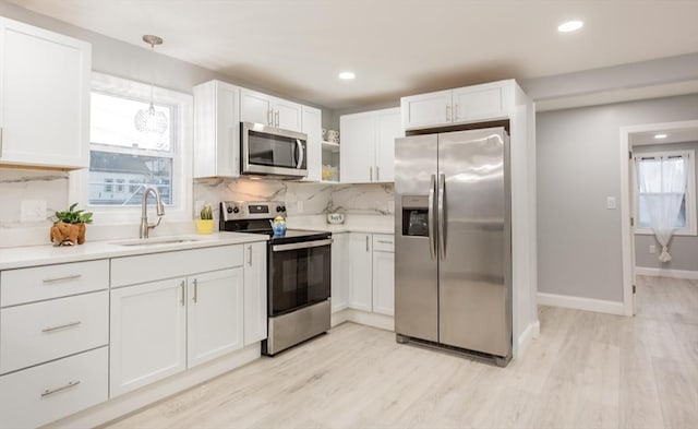 kitchen with tasteful backsplash, stainless steel appliances, sink, white cabinetry, and hanging light fixtures