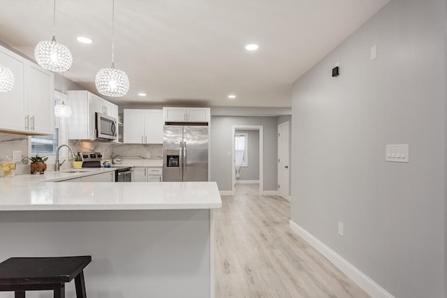 kitchen featuring hanging light fixtures, stainless steel appliances, kitchen peninsula, decorative backsplash, and white cabinets