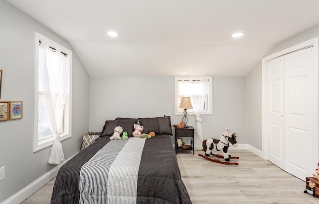 bedroom featuring multiple windows, a closet, light hardwood / wood-style floors, and vaulted ceiling