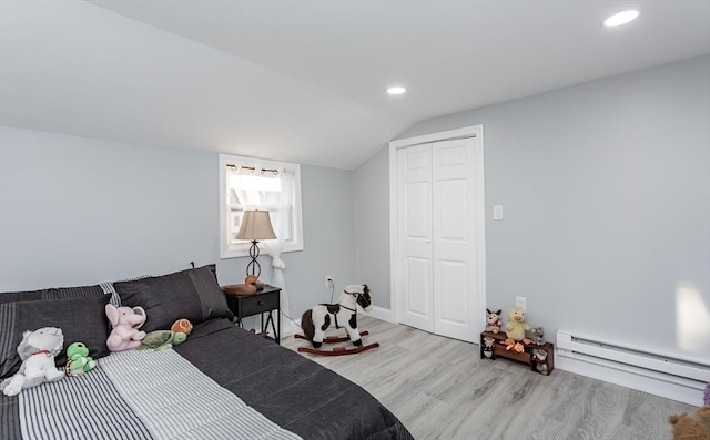 bedroom featuring lofted ceiling, light hardwood / wood-style flooring, a closet, and a baseboard heating unit