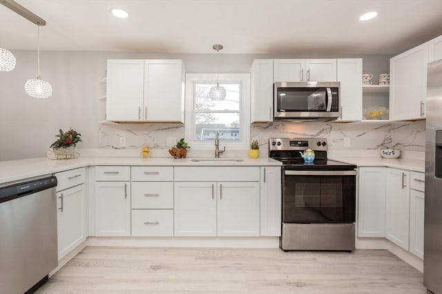 kitchen with backsplash, stainless steel appliances, sink, pendant lighting, and white cabinetry