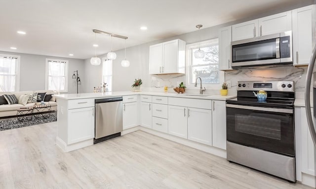 kitchen featuring kitchen peninsula, stainless steel appliances, sink, white cabinets, and hanging light fixtures