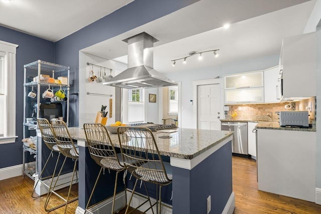 kitchen with island exhaust hood, dishwasher, backsplash, white cabinetry, and a kitchen bar