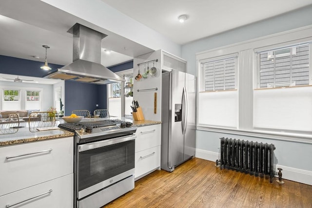 kitchen featuring radiator, stainless steel appliances, island exhaust hood, white cabinets, and baseboards