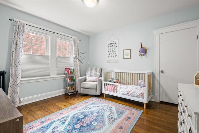 bedroom with wood finished floors, a crib, baseboards, and radiator