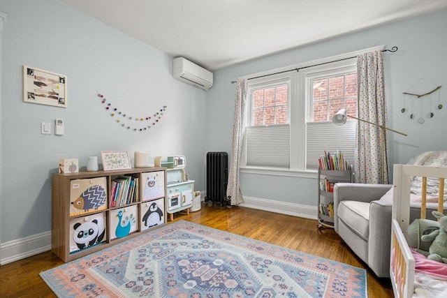 sitting room featuring radiator heating unit, a wall mounted air conditioner, baseboards, and wood finished floors
