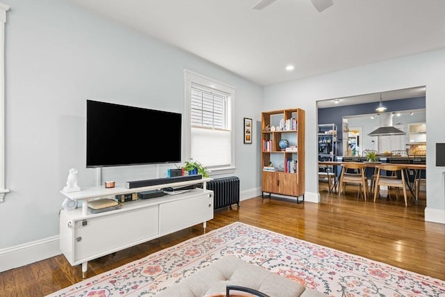 living room featuring radiator, baseboards, wood finished floors, and recessed lighting