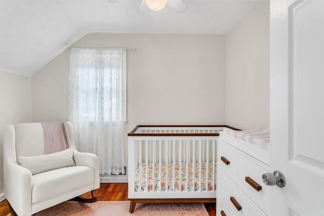 bedroom with vaulted ceiling, a nursery area, ceiling fan, and light wood-type flooring