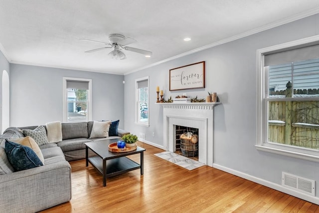 living room with ornamental molding, a tile fireplace, ceiling fan, and light wood-type flooring