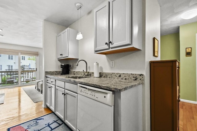 kitchen with white dishwasher, a sink, light wood-style floors, pendant lighting, and stone counters