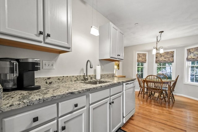 kitchen featuring white dishwasher, a sink, light wood-style floors, decorative light fixtures, and light stone counters
