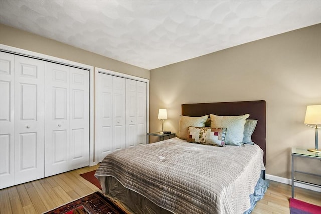 bedroom featuring two closets, wood finished floors, and baseboards
