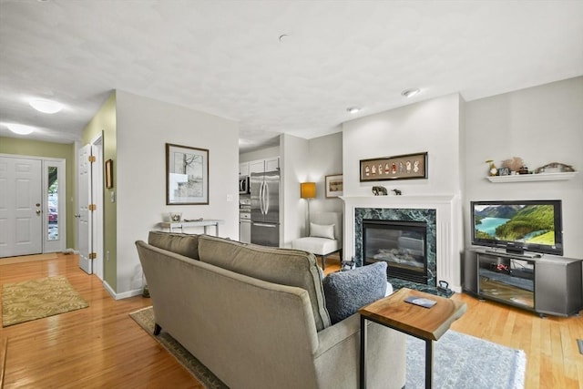 living room with light wood-style flooring, a premium fireplace, and baseboards