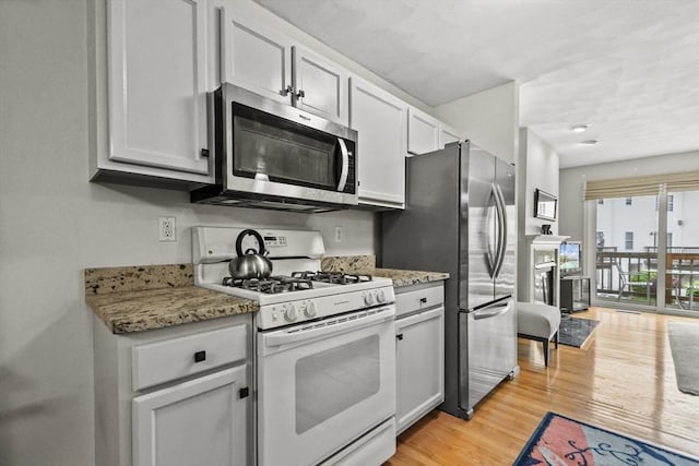 kitchen with stainless steel appliances, light wood-type flooring, and light stone counters