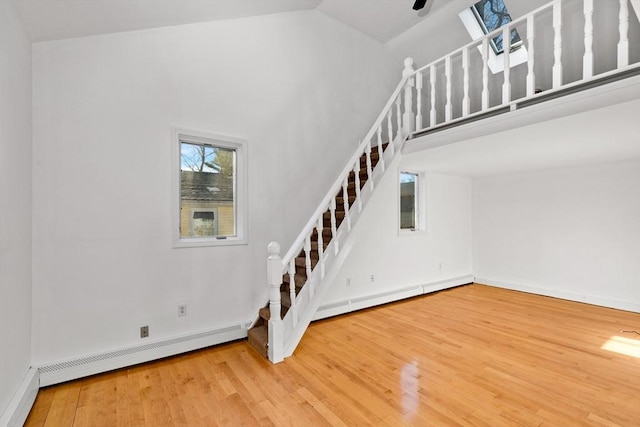 staircase with wood-type flooring, lofted ceiling with skylight, and a baseboard heating unit