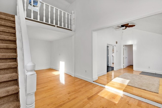 unfurnished living room with ceiling fan, hardwood / wood-style floors, and a towering ceiling