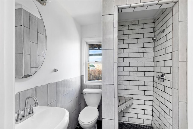 bathroom featuring toilet, a tile shower, sink, and tile walls