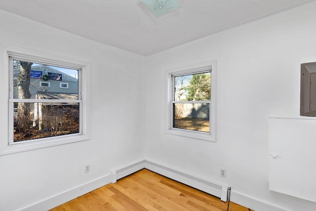 unfurnished room with hardwood / wood-style flooring, electric panel, and a baseboard heating unit