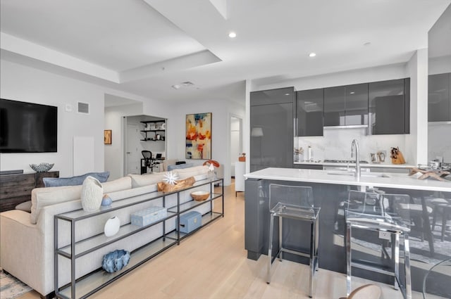 living room with sink, light wood-type flooring, and a tray ceiling