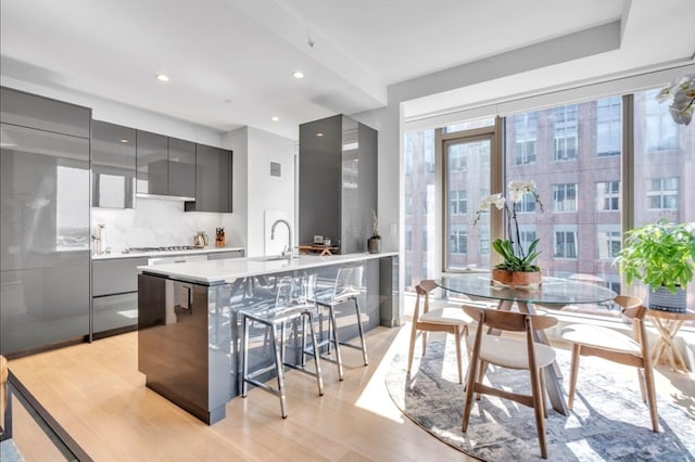 kitchen with a breakfast bar area, gray cabinets, light hardwood / wood-style floors, and tasteful backsplash