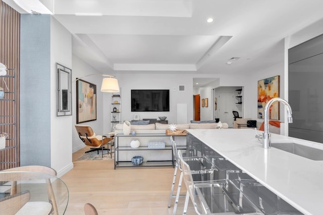 kitchen with light hardwood / wood-style floors, sink, and a tray ceiling