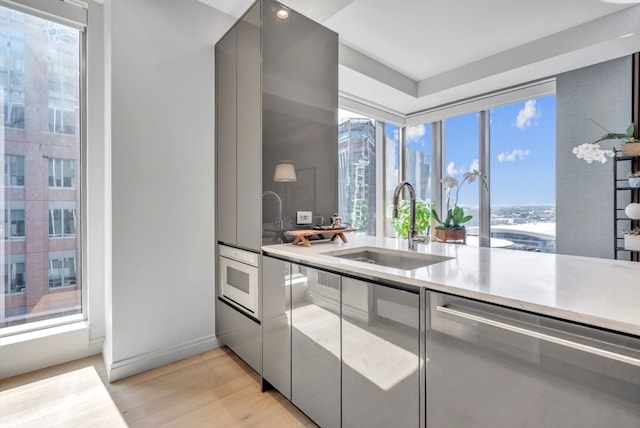 kitchen with gray cabinets, stainless steel dishwasher, sink, oven, and light hardwood / wood-style flooring