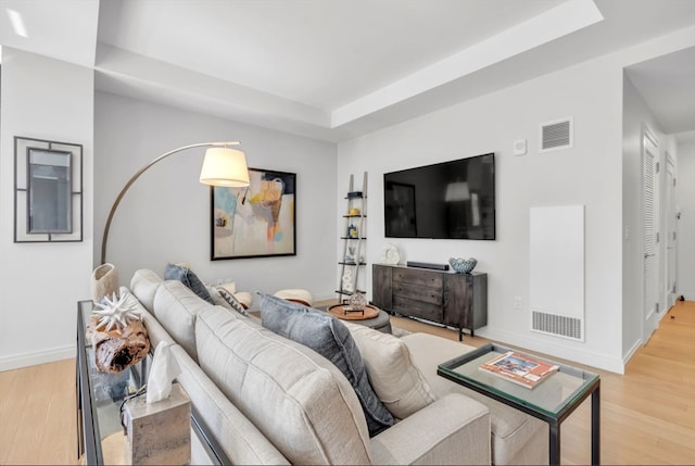 living room with a tray ceiling and light hardwood / wood-style flooring