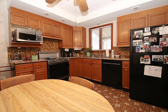 kitchen with a raised ceiling, ceiling fan, tasteful backsplash, light stone countertops, and black appliances