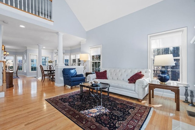 living area with baseboards, light wood finished floors, an inviting chandelier, decorative columns, and a towering ceiling