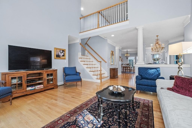 living area with a chandelier, wood finished floors, stairs, and decorative columns