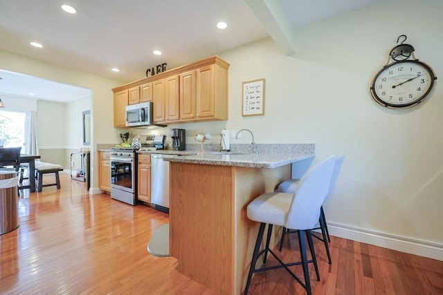 1 Washington Ct Unit 1, Uxbridge, MA 01569 - kitchen with appliances with stainless steel finishes, light brown cabinets, a kitchen bar, light wood-type flooring, and a peninsula