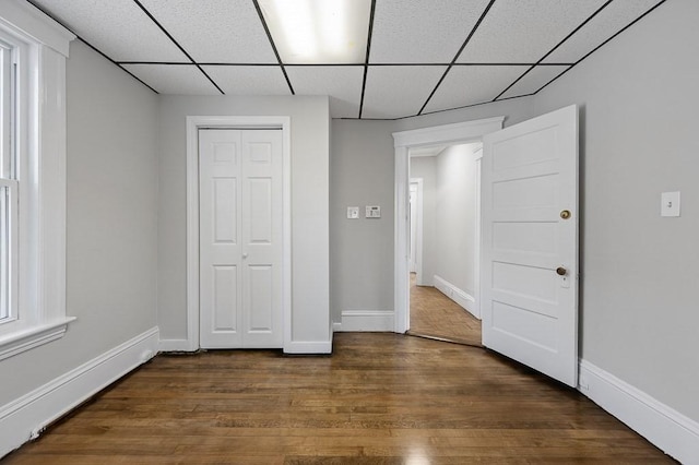 unfurnished bedroom with a drop ceiling, a closet, and dark wood-type flooring