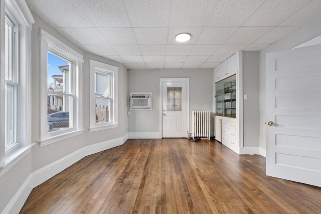 interior space featuring radiator, a drop ceiling, a wall mounted AC, and dark hardwood / wood-style floors