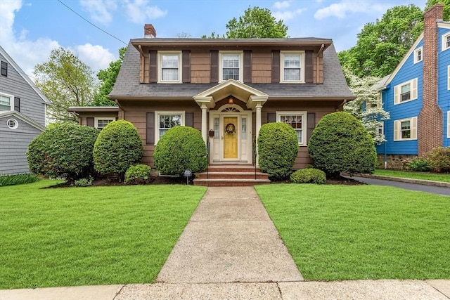 view of front of home with a front yard, a shingled roof, and a chimney
